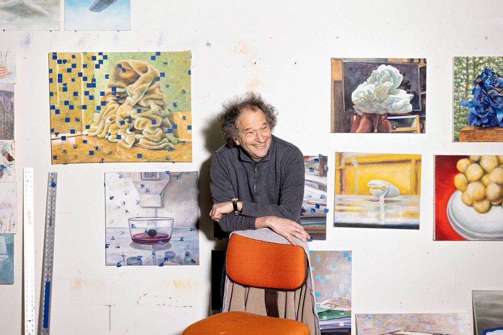 David Lefkowitz leaning against a chair in front of a wall of his paintings