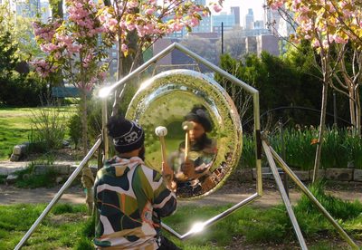 Artist seated outdoors striking a silver gong