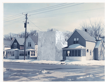 A row of plain, twp-story houses in the winter. In place of one house is a house-sized cube of snow.