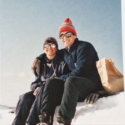 Ian Kraabel and a friend sit on a snowbank wearing sunglasses and stocking caps