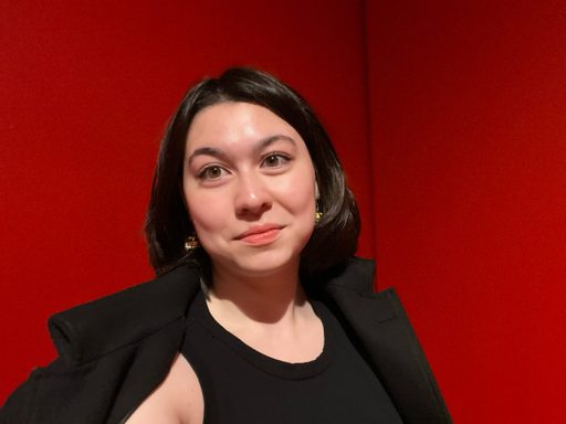 Headshot of a woman with black hair in a black dress in front of a red background