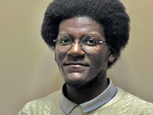 Headshot of a young man with dark skin and an afro wearing and ivory sweater