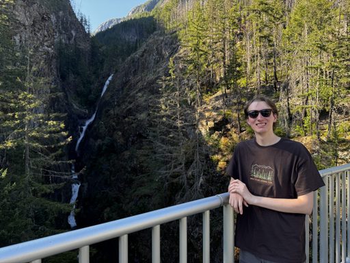 image of young man wearing a black t-shirt standing near a waterfall