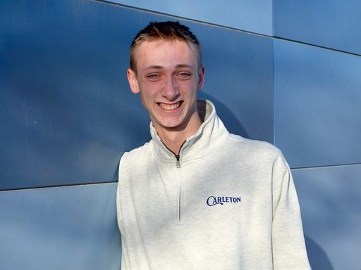 A person smiles at the camera, wearing a light gray sweatshirt with 