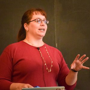 Carly wearing a red shirt and gold necklace, gesturing while giving a talk.