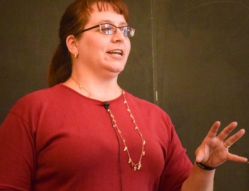 Carly wearing a red shirt and gold necklace, gesturing while giving a talk.