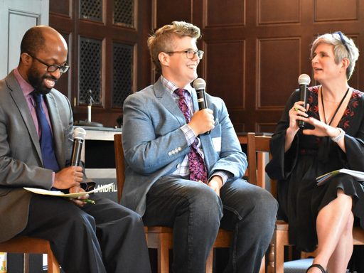 3 scholars seated on high chairs with microphones smiling and laughing during discussion.