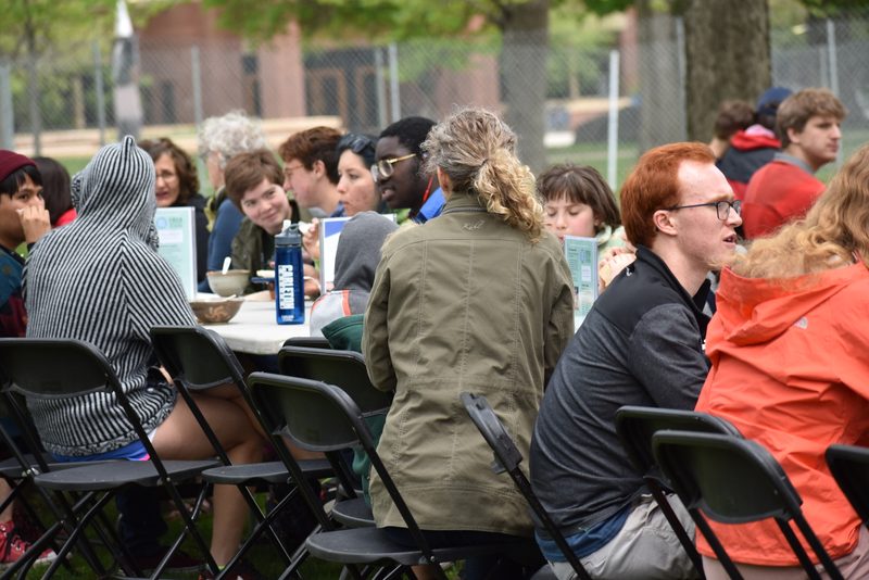 Faculty, staff, students, and community members enjoy their soup. Several people are seated outside at a long table, engaged in many conversations.