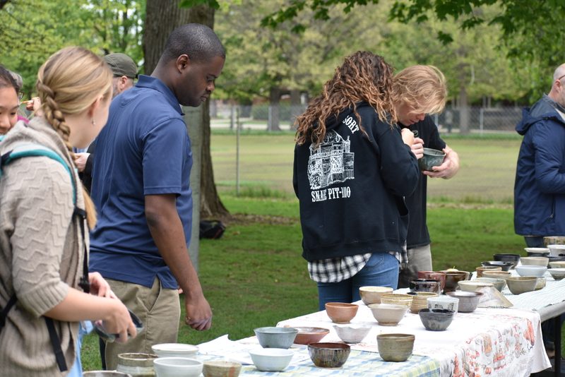 Empty Bowls 2019 attendees choose their bowls. Several individuals peruse a long table featuring many hand made clay bowls.