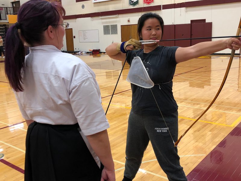 Kyudo Practice. A student draws an arrow as instructor Carly Born looks on