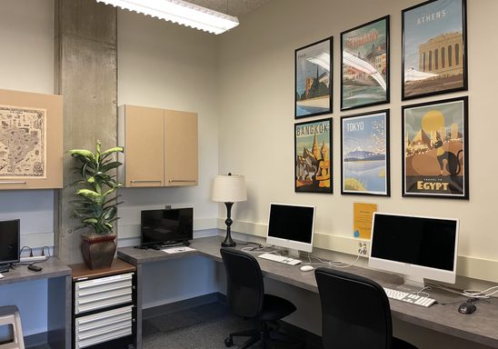 The computer lab, which contains four desks and monitors, as well as travel-inspired prints on the walls.