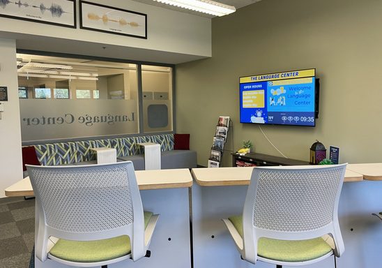 Language Center lounge taken from center of room, showing elevated tables with multilingual newsstand and Language Center television in background