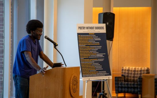 Student in a blue t-shirt and jeans stands at a podium performing a poem