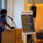 Student in a blue t-shirt and jeans stands at a podium performing a poem