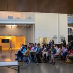 Four rows of audience members watch a student perform a poem