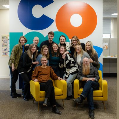 Carleton Communications staff in front of wall with COMMS in huge colorful letters