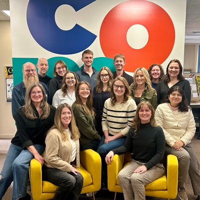 Carleton Communications staff in front of wall with COMMS in huge colorful letters