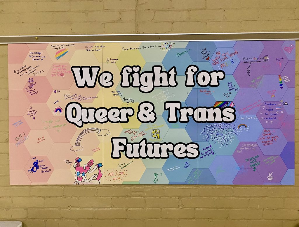 A mural reads "We fight for Queer & Trans Futures." It features doodles and encouraging words written by LGBTQIA+ students and staff.