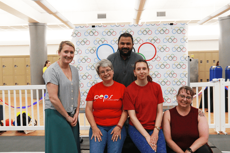 Several people standing in front of the Olympic flag