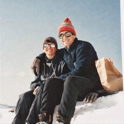 Carleton alumni Ellen Anderson Penno '84 and Ian Kraabel '85 sitting on a snowy hillside smiling at the camera