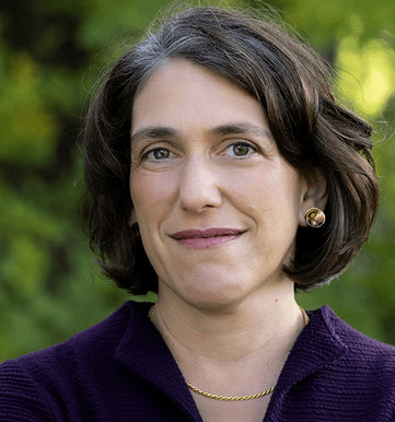 Headshot of Prof. Serena Zabin looking directly at the camera with a smile. She is wearing a dark purple top and is posed in front of greenery.
