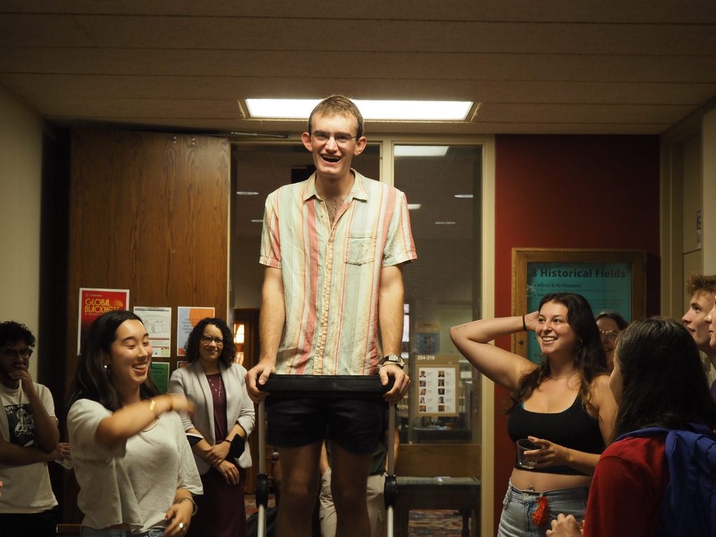 Carleton Senior Henry Moshfeghi '25 wearing a striped shirt and standing on a utility ladder introducing himself and the other History department SDAs.