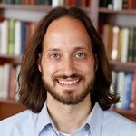 Portrait of Prof. Mason smiling in front of a book case
