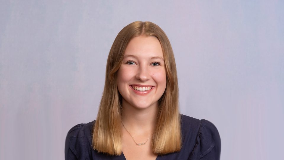 Headshot of Grace Enz '26 smiling in front of a grey backdrop and wearing a dark blouse.