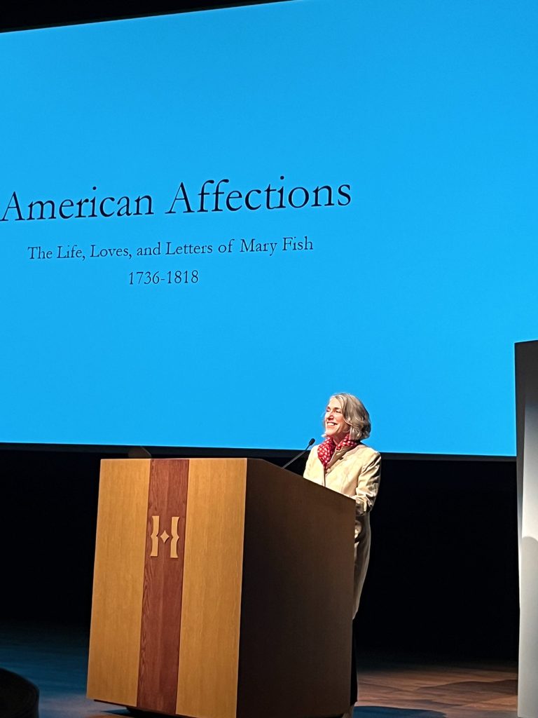 Prof. Zabin standing behind a wooden podium and in front of a blue tinted screen stating American Affections