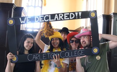 5 members of the Class of 2025 pose for a picture wearing hats, feather boas, and sunglasses with a frame that reads 