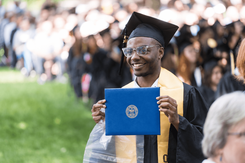 Carleton graduate holding up a diploma cover, proudly, at Commencement.
