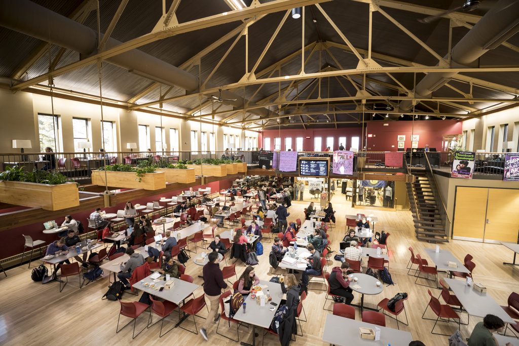 A crowd of people gather at tables for lunch in the large, vaulted space of Sayles-Hill Campus Center