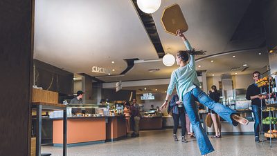 A student holding a tray dances en pointe in East Dining Hall