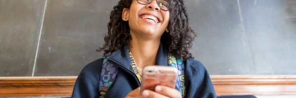 A student smiles broadly while playing on her phone