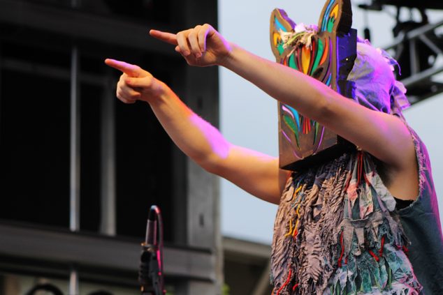 A performer dons a colorful wolf mask while playing the drums