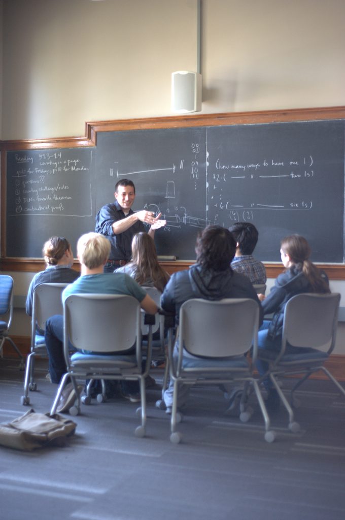 A professor in front of a blackboard, speaking to a group of seated students