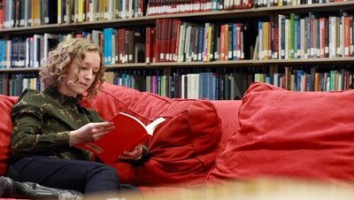 A student reads a book on a couch in Gould Library
