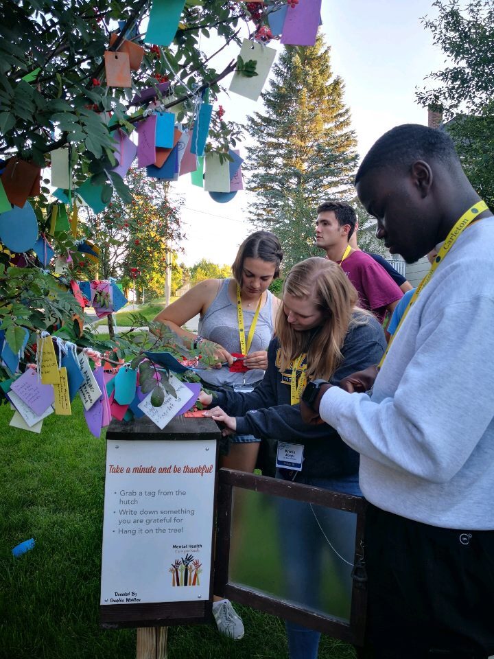 A group of students taking a minute to be thankful by writing what they are grateful for and tying it to a gratitude tree in Northfield, MN