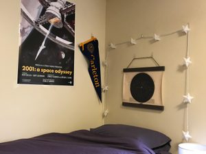 a dorm room bed, with a poster and pennant on the wall