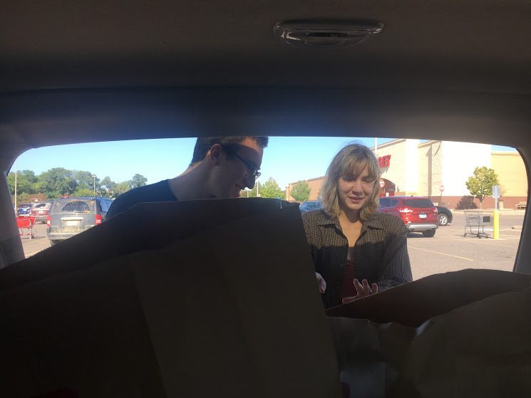 a picture through the trunk of a car looking through grocery bags at a man and a woman outside the car laughing