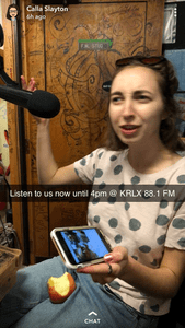 confused looking white woman speaks into a radio microphone and holds her iphone