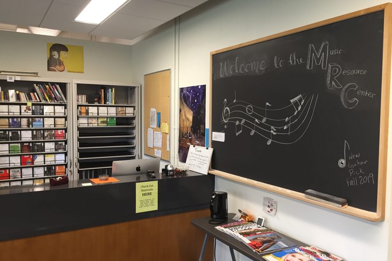 Indoor, front desk with blackboard on the side saying "welcome to Music Resource Center"