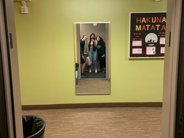Three friends pose in mirror across from elevator.