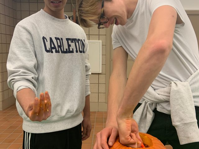 Two boys carve a pumpkin.