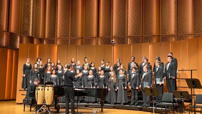 Indoor, students in Carleton Choir standing and performing on stage.