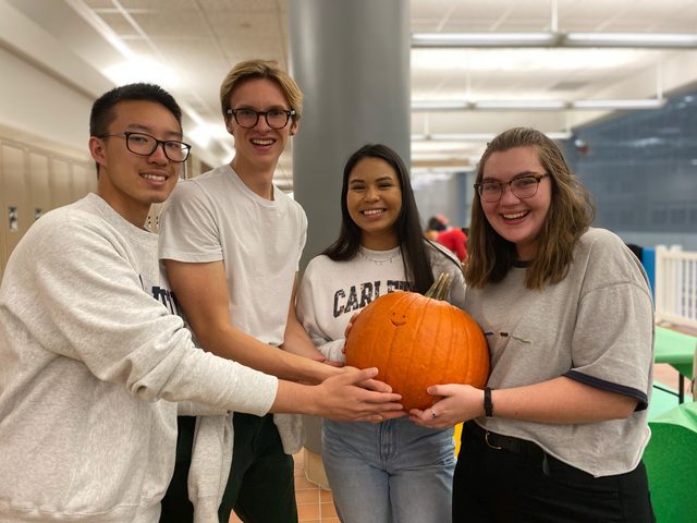 Four friends smile and hold a pumpkin