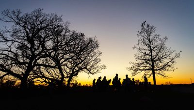 A silhouette of students at Hill of three oaks, against a sunset