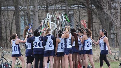 Women's Lacrosse team huddle with their sticks up