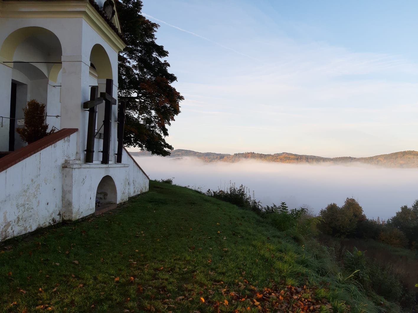 A morning view from the top of a hill shows a small church and a foggy sunrise.