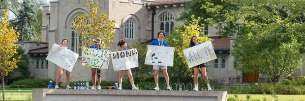 students cheering on top of carleton sign during move-in